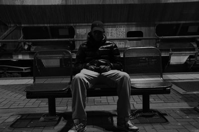 男子坐在金属长凳上的灰度照片